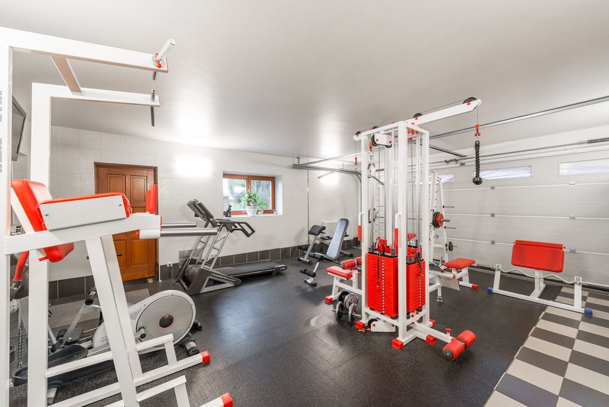 Home gym residencial completo e iluminado com rack, esteira, bicicleta e banco